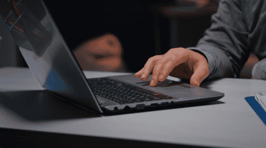 man in a gray shirt holding his hand on an opened laptop
